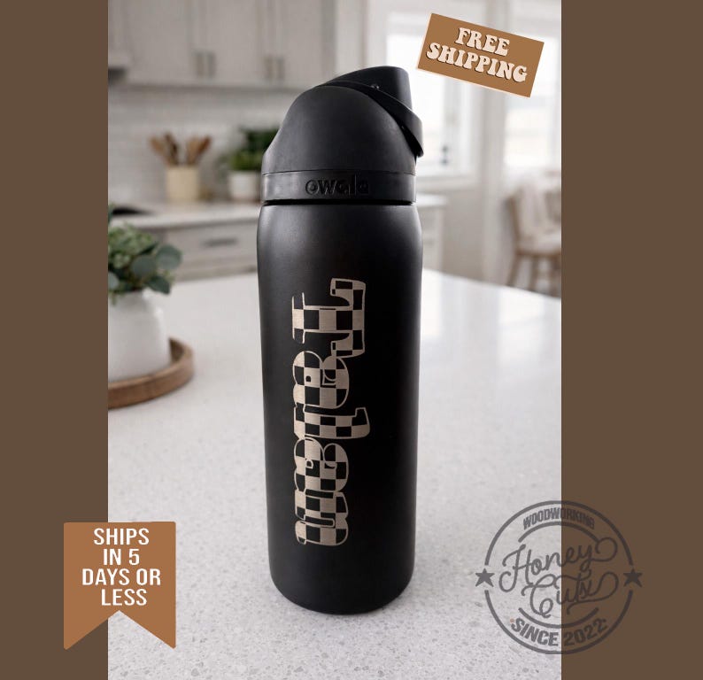 K&ouml;nnte beinhalten: Eine schwarze Owala-Wasserflasche mit einem karierten "Tabitha"-Design. Die Flasche hat einen schwarzen Griff und Deckel. Die Flasche steht auf einer wei&szlig;en Arbeitsplatte. Das Bild enth&auml;lt auch den Text "Versand in 5 Tagen oder weniger" und "Kostenloser Versand".