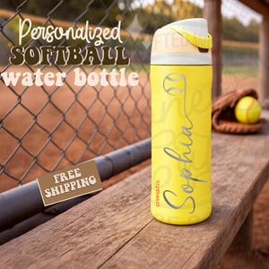 K&ouml;nnte beinhalten: Gelbe Softball-Wasserflasche mit wei&szlig;em und gelbem Deckel. Die Flasche hat eine Softball-Grafik und den Namen "Sophia" in Schreibschrift. Im Hintergrund steht "Personalized Softball Water Bottle".