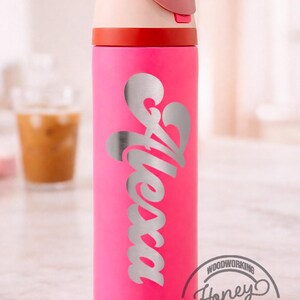 K&ouml;nnte beinhalten: Eine pinkfarbene Wasserflasche mit dem Schriftzug "Alessa" in Silber. Der Deckel ist rosa und cremefarben, mit einem roten Band. Das "Honey Cuts" Logo ist sichtbar.