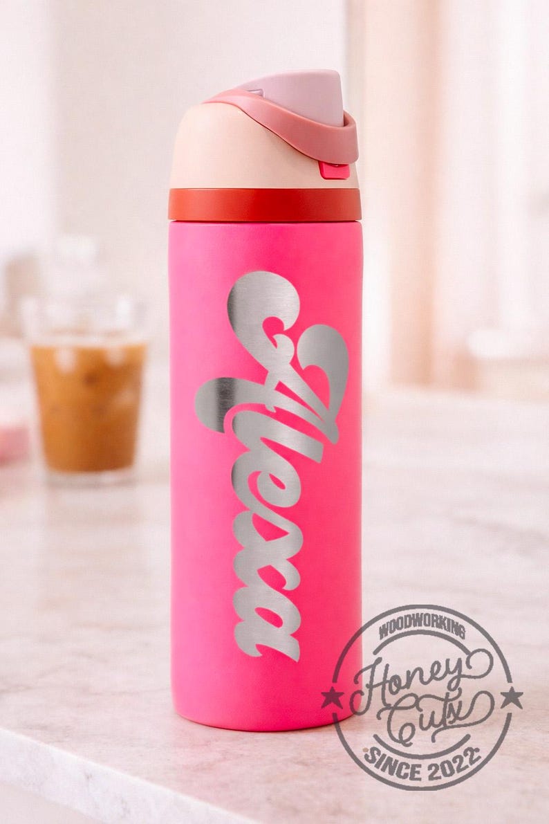 K&ouml;nnte beinhalten: Eine pinkfarbene Wasserflasche mit dem Schriftzug "Alessa" in Silber. Der Deckel ist rosa und cremefarben, mit einem roten Band. Das "Honey Cuts" Logo ist sichtbar.
