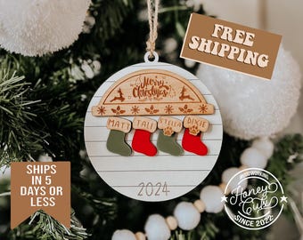May include: A white wooden Christmas ornament with a red and green stocking design. The ornament features the names Matt, Tali, Stella, and Dixie, along with the year 2024. The ornament is decorated with a wooden arch that says "Merry Christmas".