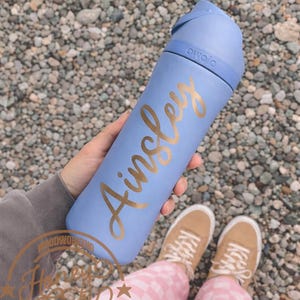 Op de afbeelding: Een witte keramische mok met een zwart handvat en de tekst "But First, Coffee" in een zwarte, vette letter. De mok staat op een houten oppervlak.