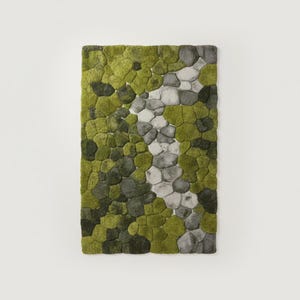 May include: A rectangular rug with a textured surface, featuring a pattern of green, gray, and white shapes resembling stones. The rug's design includes varying shades of green, with a central line of gray and white stones.
