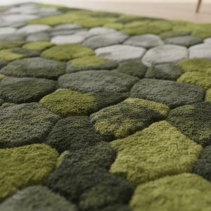 May include: A textured rug with a stone-like pattern in shades of green and gray. The rug's design features rounded, irregular shapes, creating a natural, organic aesthetic. The varying shades of green and gray add depth and dimension to the rug.