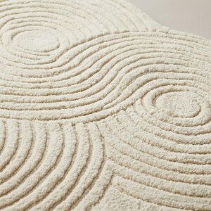 Close-up of soft wool tufted pile showing carved sculpted loop and cut texture with raised topographic ripple detailing in cream ivory