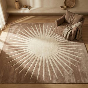 Könnte beinhalten: Ein großer, rechteckiger Teppich mit einem Sonnenstrahl-Design. Der Teppich hat eine hellbeige Mitte mit strahlenförmigen Linien in einer dunkleren Beige-Farbe. Er liegt auf einem Holzboden, mit einem braunen Sessel und einer Decke im Hintergrund.