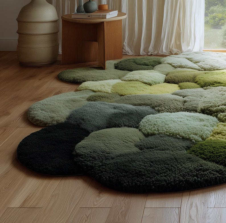 Op de afbeelding: Een zacht, abstract tapijt in groentinten, van diep bosgroen tot licht chartreuse. Het ontwerp van het tapijt bestaat uit overlappende, organische vormen, waardoor een getextureerd, gelaagd effect ontstaat. Het tapijt ligt op een lichtgekleurde houten vloer.