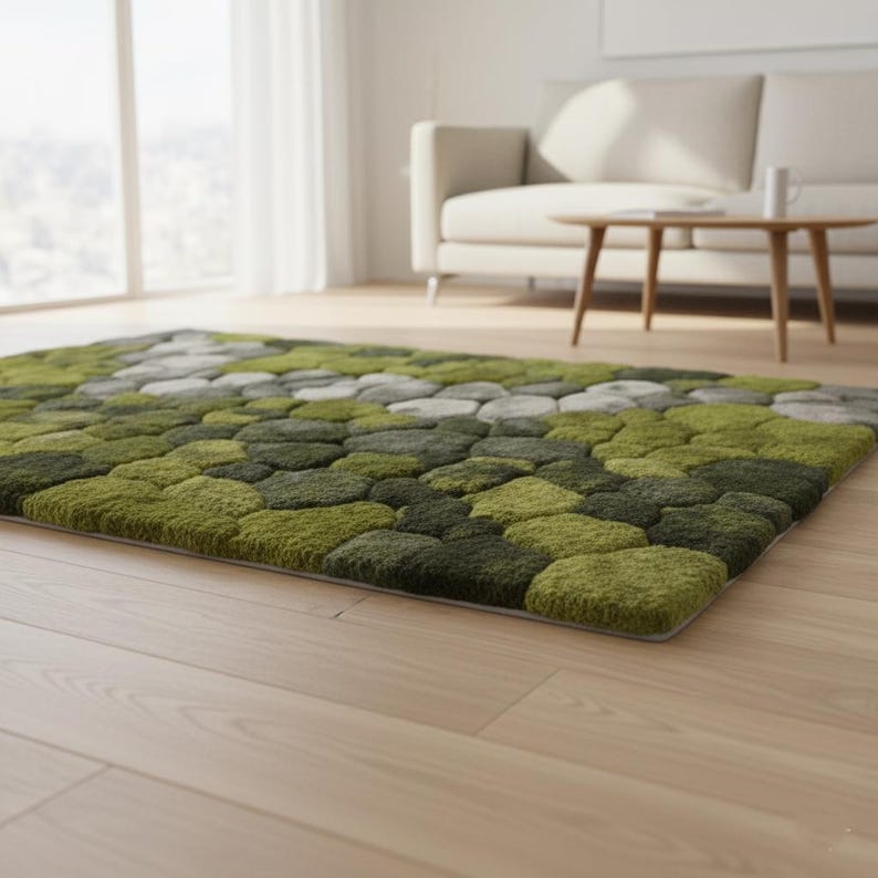 May include: A rectangular area rug with a textured, pebble-like design in shades of green and gray. The rug is placed on a light-colored wooden floor, with a sofa and coffee table in the background. The rug's dimensions are approximately 60 x 96 inches.
