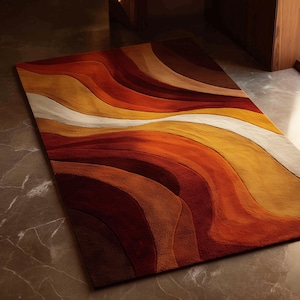 Puede incluir: Una alfombra rectangular con un patrón ondulado en tonos de rojo, naranja, amarillo y blanco. El diseño de la alfombra se asemeja a olas superpuestas. Está colocada sobre un suelo de mármol.