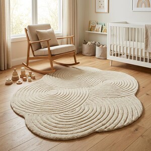 May include: An off-white, cloud-shaped area rug featuring a textured, raised pattern of concentric circles and swirling lines. The rug has a soft, tufted pile and an irregular, organic outline that covers a portion of the wooden floor.