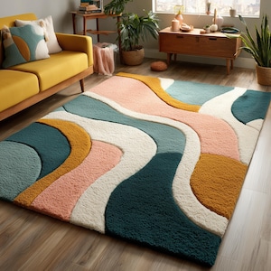Peut inclure: Un tapis de sol coloré avec un motif abstrait et ondulé. Le tapis présente des couleurs teal, rose, blanc et jaune moutarde. Il est posé sur un sol en bois dans un salon, avec un canapé jaune et des plantes en arrière-plan.