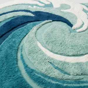 May include: A round, textured rug with a wave design. The rug features shades of blue, teal, and white, creating a swirling pattern. The design is raised, adding dimension and texture to the rug. The rug is made of a soft, plush material.
