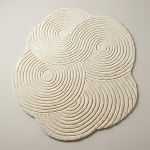 Modern sculpted hand tufted area rug with abstract curved line design and freeform shape placed on wooden flooring