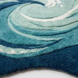 May include: A plush, round rug with a swirling wave design. The rug features shades of blue, teal, and white, creating a textured, ocean-inspired pattern. The rug's design evokes the movement of water.