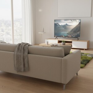 May include: A modern living room featuring a beige sofa with a gray throw blanket. A large flat-screen TV displays a mountain landscape. The room includes a wooden coffee table, a white and wood TV stand, and a green rug.