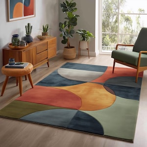 Könnte beinhalten: Moderner Teppich mit abstraktem Design in einem Wohnzimmer. Der Teppich zeigt große, sich überlappende Formen in Blau-, Orange-, Gelb-, Grün- und Grautönen. Er liegt auf einem hellen Holzboden.