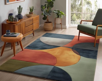 May include: A colorful area rug with an abstract geometric design. The rug features large, overlapping shapes in shades of blue, orange, yellow, green, and gray. The rug is placed on a light-colored wooden floor in a living room setting.