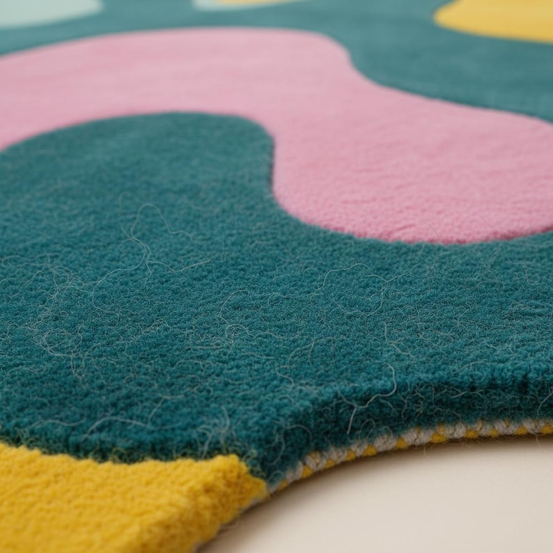 K&ouml;nnte beinhalten: Nahaufnahme eines farbenfrohen Teppichs mit abstraktem Design. Der Teppich hat einen tealfarbenen Hintergrund mit gro&szlig;en, unregelm&auml;&szlig;igen Formen in Rosa und Gelb. Die Textur des Teppichs wirkt weich und pl&uuml;schig, mit sichtbaren Fasern.