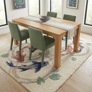 May include: A light wood dining table with four green chairs. A cream-colored rug with koi fish and lily pads is under the table. A blue and white striped table runner and a blue bowl are on the table.