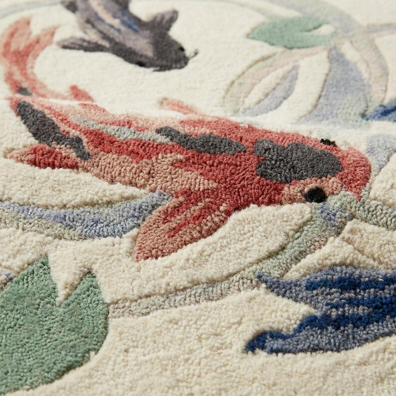 May include: Close-up of a textured rug featuring a koi fish design. The rug showcases a cream background with a red, pink, and gray koi fish. Additional details include blue, green, and gray water plants, creating a serene aquatic scene.