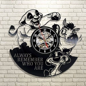 Peut inclure: Horloge en vinyle noir représentant une silhouette de Simba et Pumbaa du film d'animation Le Roi Lion de Disney. Le cadran de l'horloge est un cercle blanc avec des chiffres et des aiguilles noirs. L'horloge porte la citation "Always remember who you are" imprimée dessus.