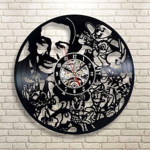 以下が含まれることがあります： ウォルト・ディズニーとミッキーマウス、ドナルドダック、グーフィーなど、さまざまなディズニーキャラクターのシルエットが描かれた黒いビニールレコードの時計。時計は銀色の文字盤で、黒い数字と針があります。