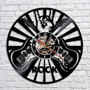 Puede incluir: Reloj de vinilo negro con un signo de paz y dos guitarras eléctricas. La esfera del reloj tiene un diseño de engranaje y las palabras "ROCK" están impresas debajo de la esfera del reloj.