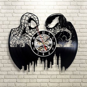 Pode incluir: Relógio de vinil preto com uma silhueta do Homem-Aranha e Venom sobre um fundo de cidade. O mostrador do relógio é branco com números e ponteiros pretos.