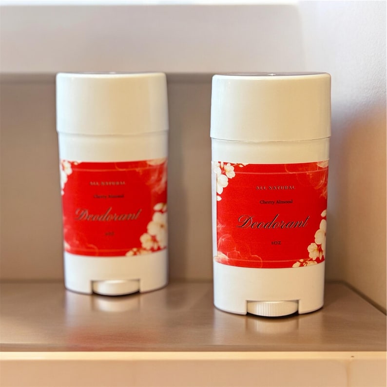 Puede incluir: Dos envases de desodorante blancos con etiquetas rojas. Las etiquetas presentan un dise&ntilde;o floral y el texto "All Natural Cherry Blossom Deodorant".
