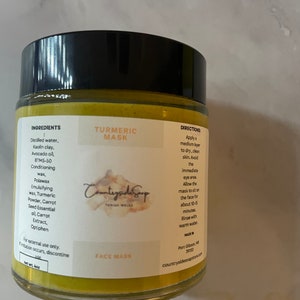Könnte beinhalten: Ein gelbes Glas mit schwarzem Deckel, beschriftet mit "Kurkuma Maske", mit den Zutaten und Anweisungen auf der Seite. Das Glas ist mit "Countryside Soap" und "Gesichtsmaske" beschriftet.