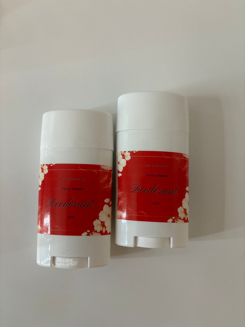 Puede incluir: Dos barras de desodorante blancas con etiquetas rojas y blancas. Las etiquetas dicen "All Natural" y "Cherry Almond Deodorant" con un dise&ntilde;o floral. Las barras son de 2 oz cada una.