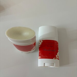 Puede incluir: Un stick de desodorante blanco con una etiqueta roja que dice "All Natural Cherry Almond Deodorant 3 oz". La etiqueta tiene un dise&ntilde;o floral con flores blancas sobre un fondo rojo.