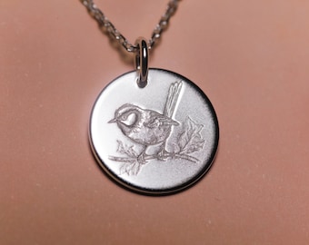 Peut inclure: Un collier en argent avec un pendentif rond représentant une petite gravure d'un oiseau perché sur une branche.