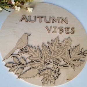 May include: A round wooden sign with the text "AUTUMN VIBES" in cutout letters. A bird is perched on a branch with leaves.