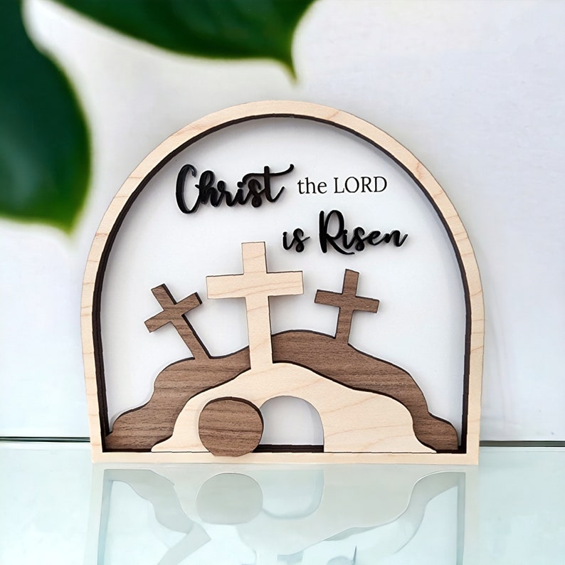 May include: Wooden Easter sign with a brown and white archway, three crosses, and the text "Christ the LORD is Risen".