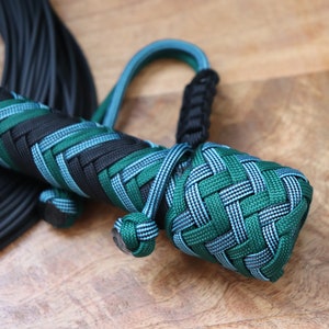 May include: A close-up of a braided whip handle with a green, blue, and black color scheme. The handle is made of paracord and has a knot at the end.