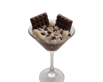 May include: A chocolate dessert in a martini glass. The dessert has a chocolate base, whipped cream, chocolate chips, and two chocolate waffle pieces. The glass has a clear stem and base, against a white background.