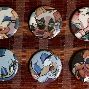 May include: Set of six round pinback buttons featuring cartoon characters with various expressions and poses. The buttons have a colorful design with shades of blue, pink, and brown. The text "AN THAT TRACKS" is on one button.