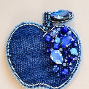 Könnte beinhalten: Eine blaue Jeans-Apfelbrosche mit silbernem Rand und blauen und hellblauen Strasssteinen.