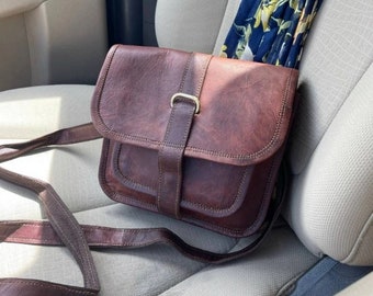 May include: A brown leather crossbody bag with a flap closure and a gold buckle. The bag has a long adjustable strap and a smaller pocket on the front.