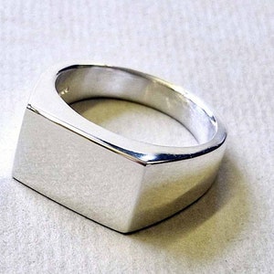 May include: A silver signet ring with a flat, rectangular top.