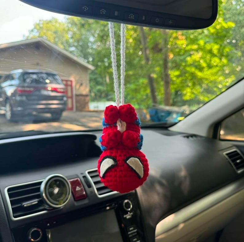 Puede incluir: Un personaje de Spiderman de crochet rojo y azul colgando de un espejo retrovisor en un coche.