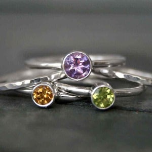 Può includere: Primo piano di diversi anelli d'argento con pietre preziose colorate. Gli anelli presentano una pietra preziosa viola, gialla e verde. Gli anelli sono impilati uno sull'altro, con le pietre preziose rivolte verso l'alto.