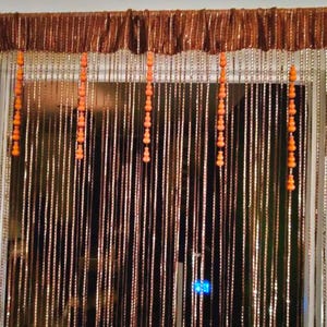 May include: A decorative beaded curtain with a brown valance. The curtain features long, vertical strands of beads in shades of brown and white, with orange beaded accents. The curtain is designed to hang in a doorway or window.