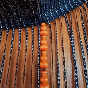 May include: An orange, decorative beaded curtain with a series of rounded shapes. The curtain hangs in front of a wooden surface. The top of the curtain is black with vertical strands of black and silver beads.