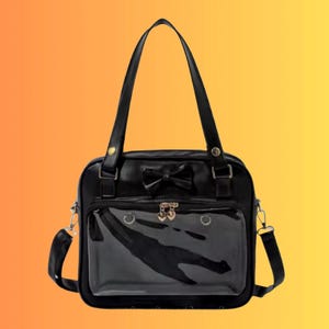 May include: Black satchel bag with a bow detail and a clear front pocket. The bag has a top handle and a detachable shoulder strap. Gold-coloured heart-shaped charms adorn the clear pocket. The bag is set against a gradient orange and yellow background.