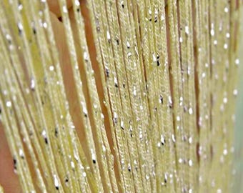 May include: Close-up of a yellow curtain with silver metallic accents. The curtain is made of numerous vertical strands, creating a shimmering effect. The strands are closely spaced, and the silver accents are irregularly distributed.