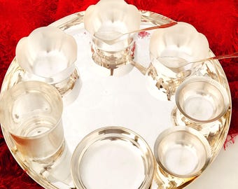 May include: A silver serving platter with various compartments, including bowls and a small plate. The tray is set against a red, fluffy fabric. The tray has a shiny, reflective surface.
