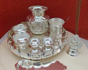 Puede incluir: Un juego ceremonial de plata con una bandeja, una jarra, cuencos, una cuchara, un diya y varillas de incienso. El juego está decorado con intrincados diseños florales y geométricos.