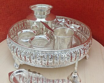 May include: A silver-plated tray with an ornate design, featuring a small silver jug, a cup, and several small bowls. The tray has four legs and is decorated with intricate patterns. There is also a small silver bell and a silver spoon.